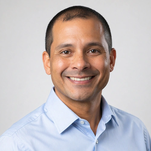 Professional headshot of smiling man in light blue shirt against neutral background